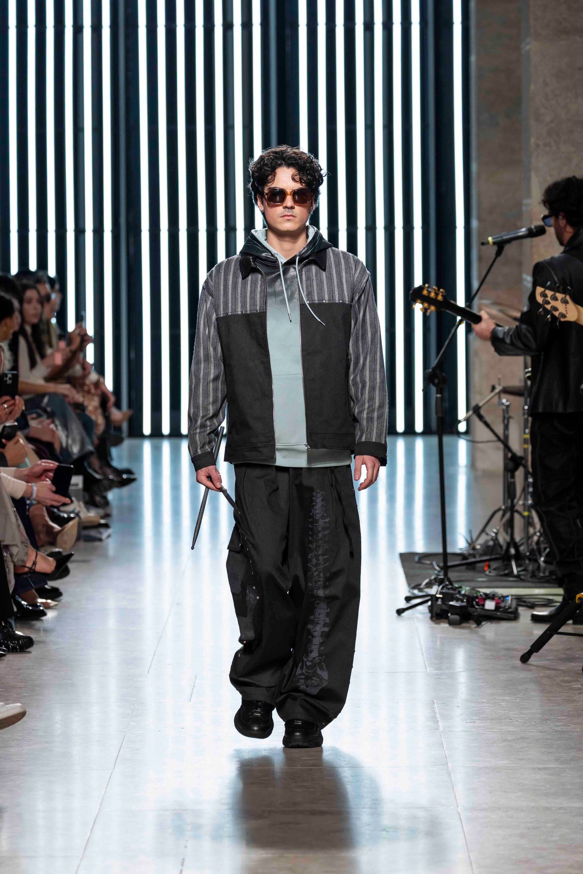 Runway look with the Smoked Green Sweater layered under a striped jacket and worn with black trousers
